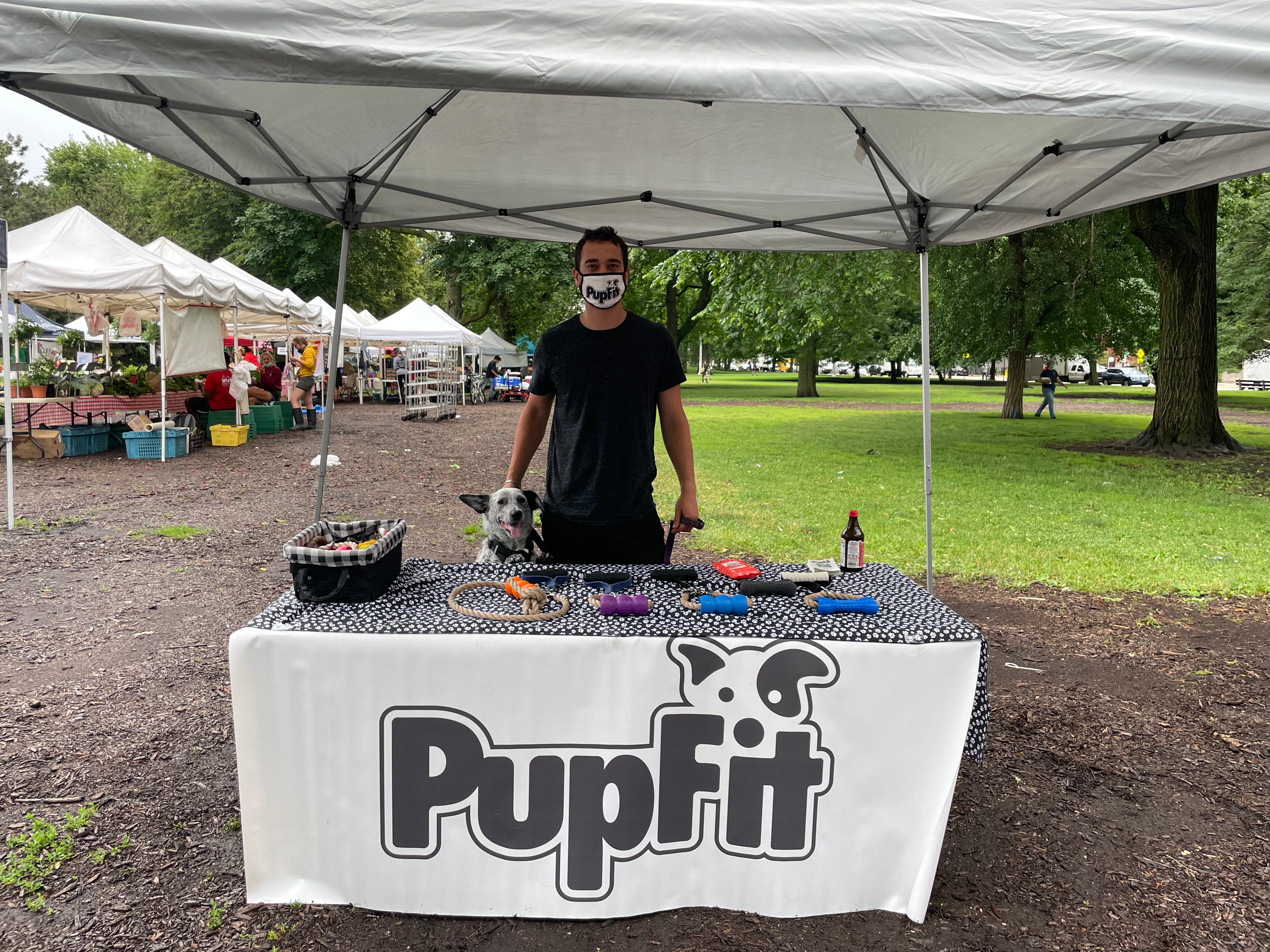Person with a dog at a 'PupFit' table under a tent in an outdoor setting