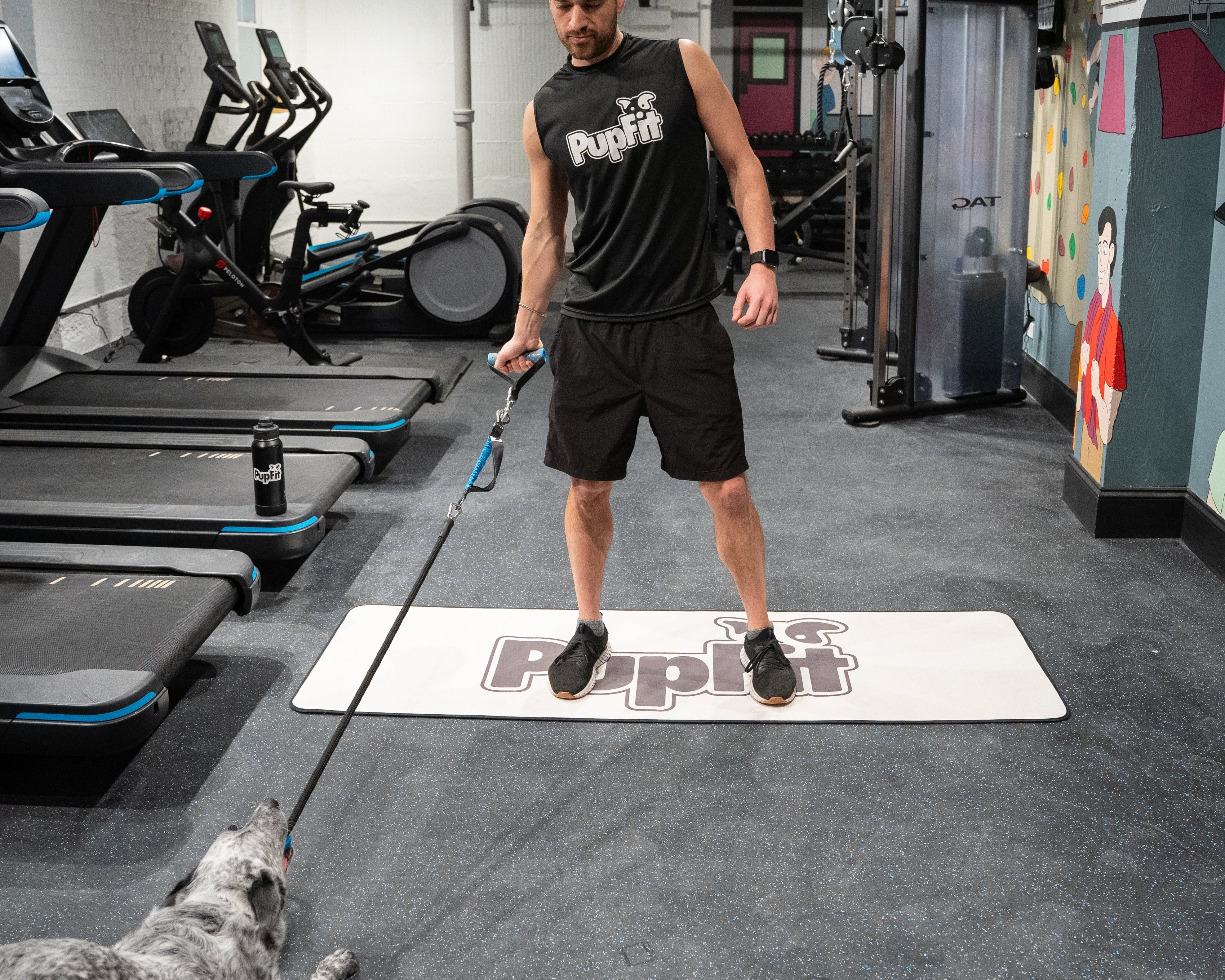 Man exercising with a pupfit resistance tug toy on a mat in a gym setting