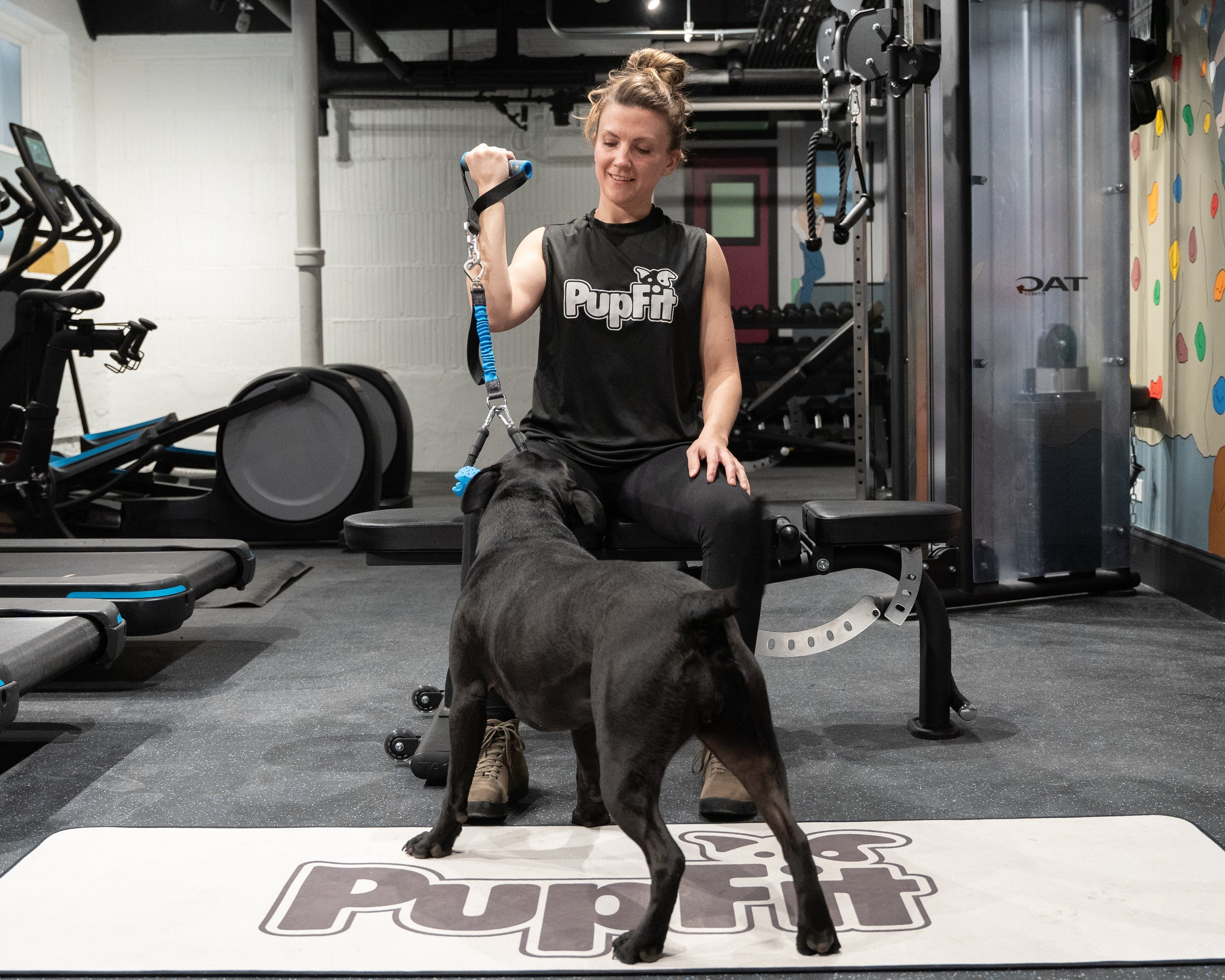 Woman exercising with a dog and pupfit tug toy on a mat in a gym setting
