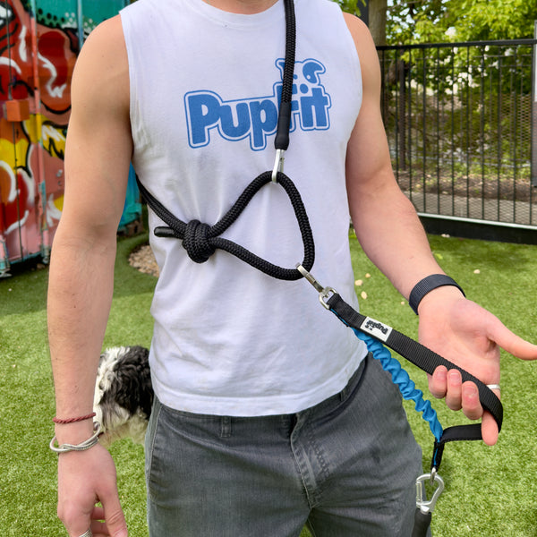 Person wearing a 'PupFit' shirt holding a dog leash with a dog in the background