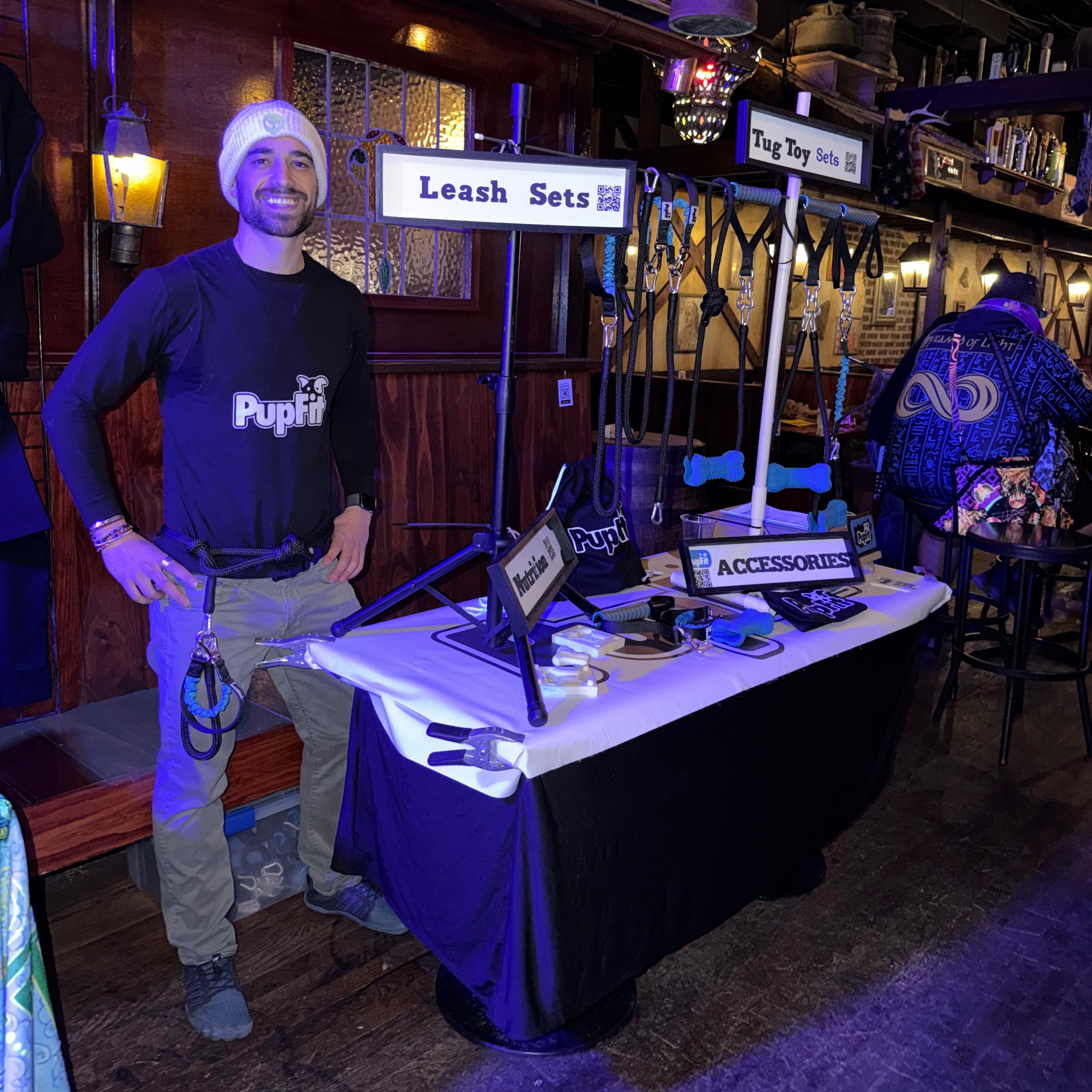 Person standing next to a table with PupFit gear in a dimly lit room.