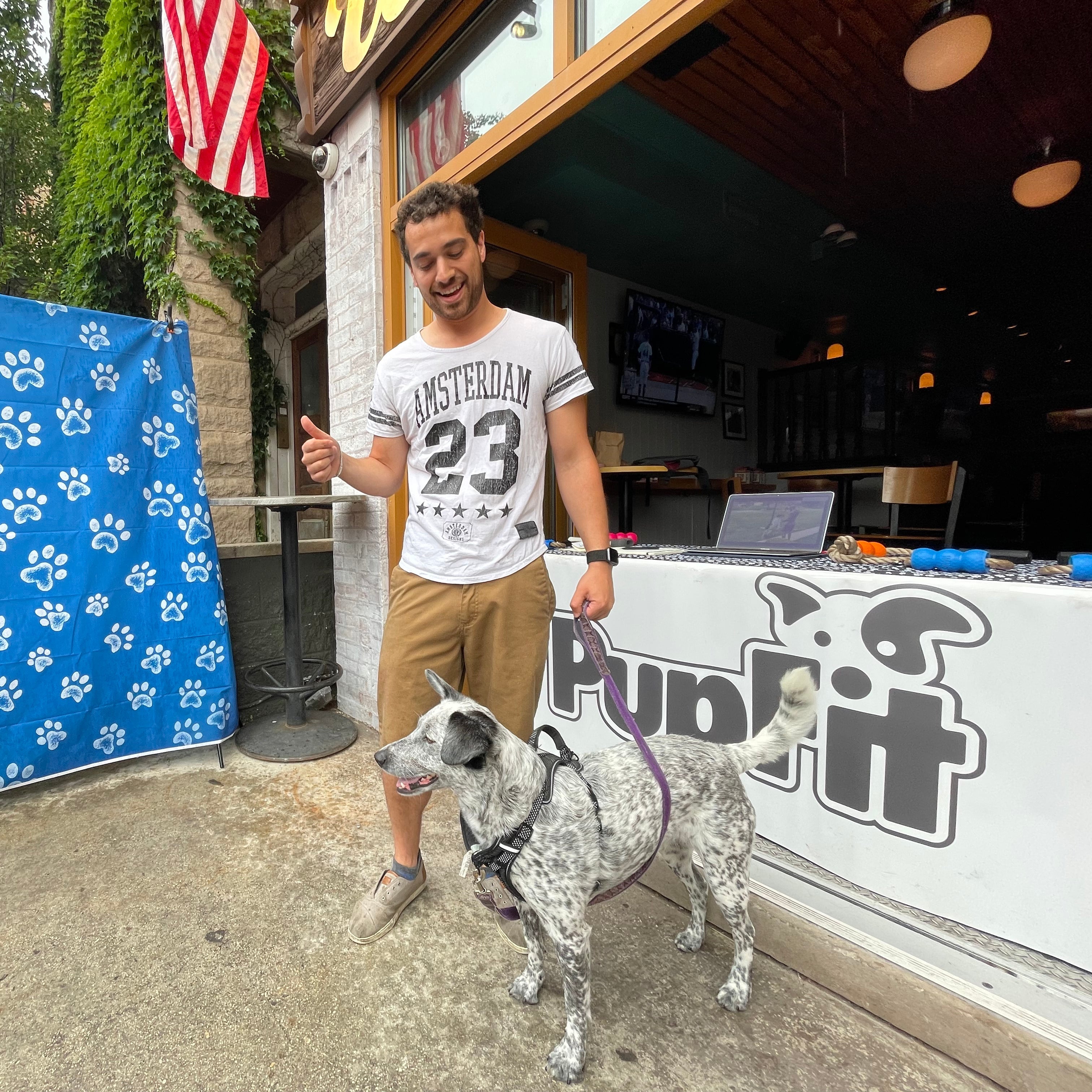 Man with a dog standing in front of Woodies Flat with 'PupFit' branding